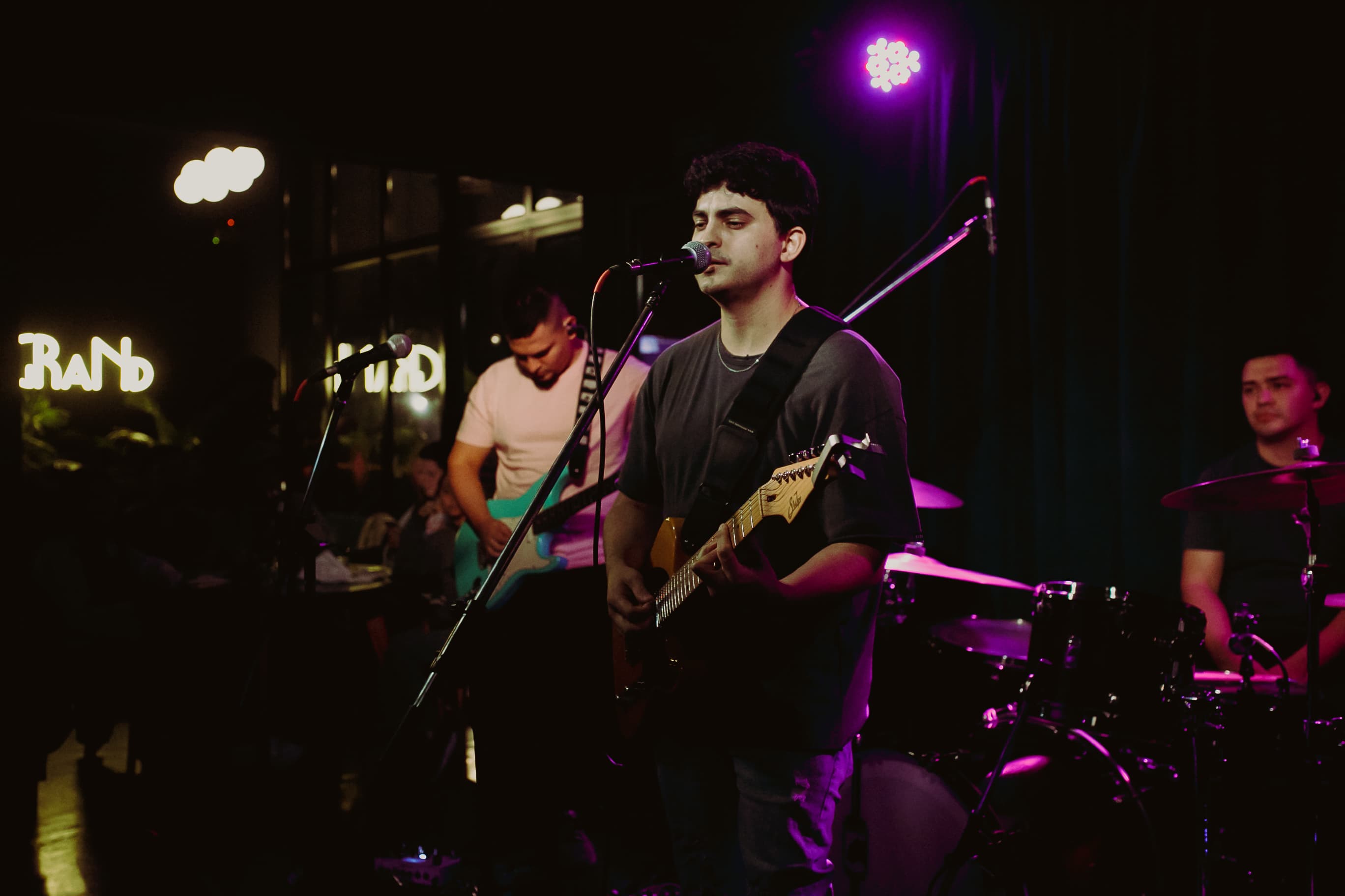 Proverbs performing live at Bar Legrand, with guitars, vocals and drums under purple stage lights.