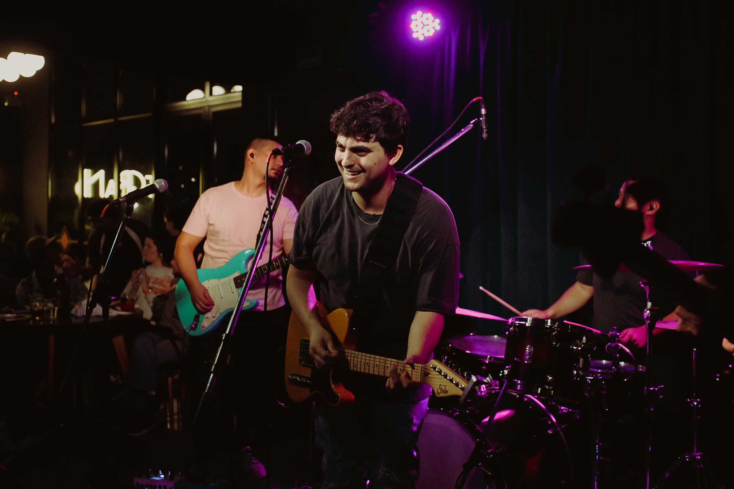 The Proverbs singer playing guitar at the front of the stage, with the guitarist and drummer behind him.